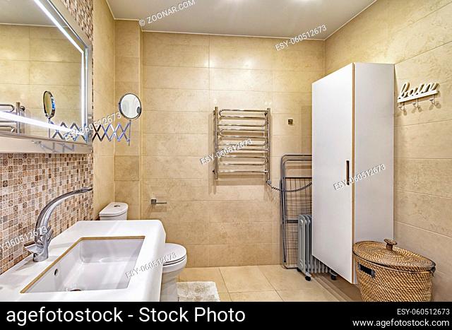 modern bath, mirror, toilet and ceramic sink in beige tiled spacious neat bathroom