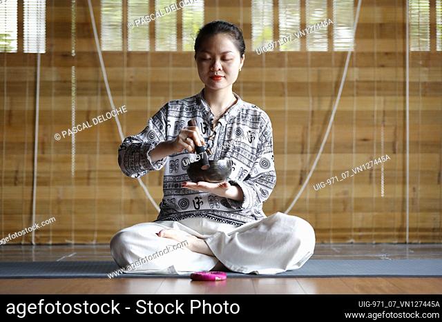 Buddhist woman holding and playing a tibetan singing bowl with a wooden stick. Tibetan bowl is used in sound therapy, meditation and yoga. Vietnam