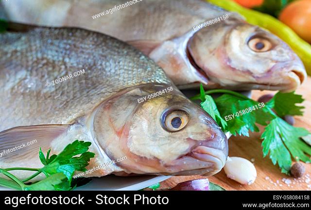 On the plate are two large bream. Nearby are vegetables and spices for cooking this river fish. Front view, close-up
