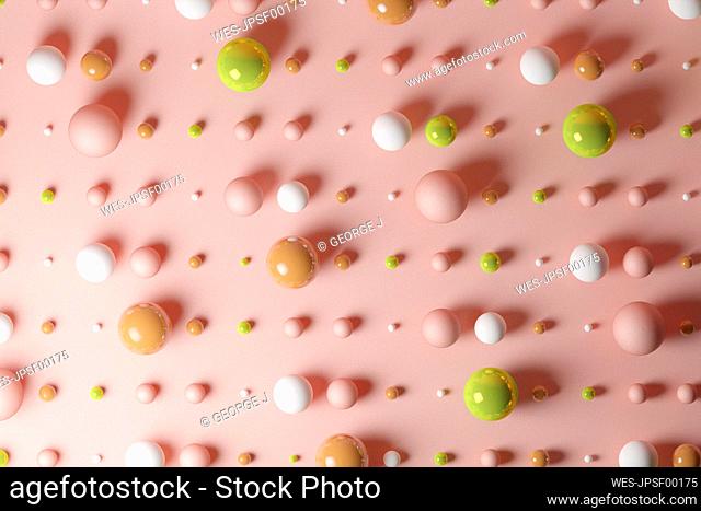 Three dimensional pattern of various spheres flat laid against pink background