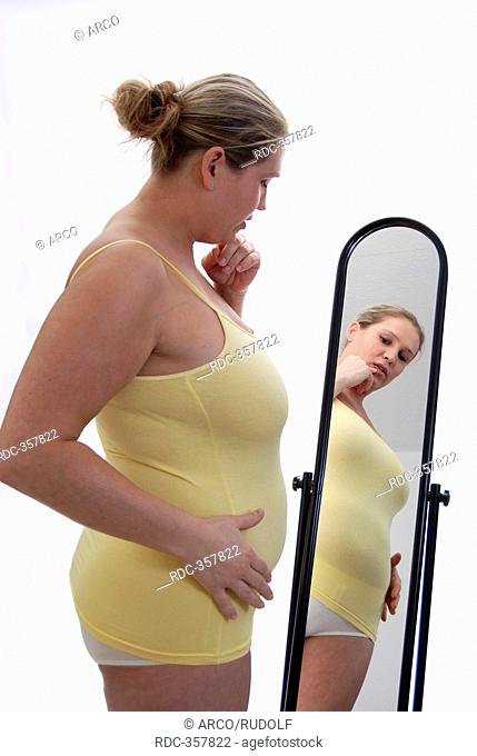 Chubby woman with big belly in front of mirror, looking at her physique