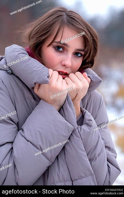 young woman on winter nature freezes with covered face, looking at camera