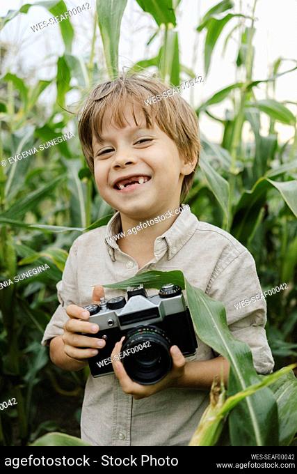 Smiling boy standing with vintage camera in corn field