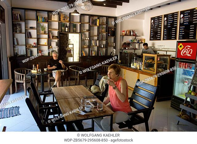A tourist (Model Release 20020923-10) is enjoying coffee in one of the numerous coffee houses in the UNESCO world heritage town of Luang Prabang in Central Laos