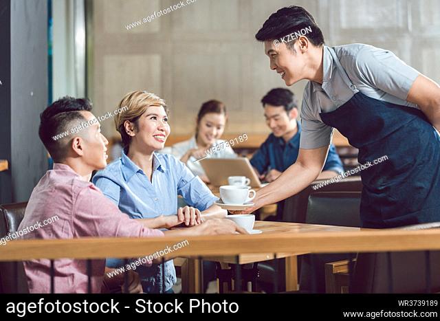 Young smiling couple being served with coffee at table in the cafe