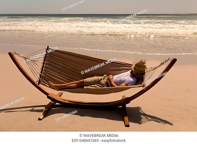 Young man with hat and hand behind hand relaxing on hammock at beach