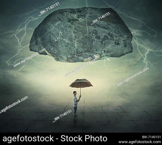 Surrealistic image as a man stand in a foggy street under a huge levitating rock, holding an umbrella in hand as a protection from danger