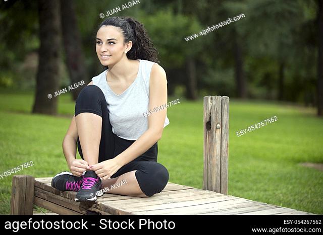 Portrait of cheerful sportswoman tying laces on sneakers in park
