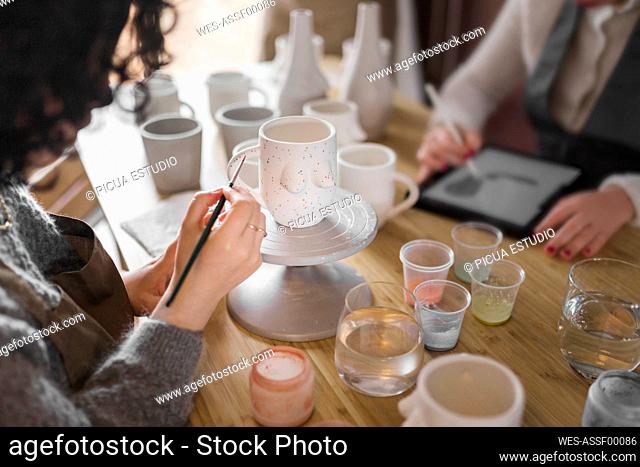 Female artist painting cup while working with colleague at workshop