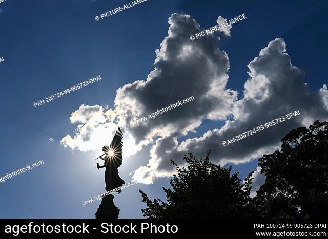21 July 2020, Berlin: The sun is shining through a gap on an angel figure in the garden of Charlottenburg Palace under a blue sky with prominent clouds