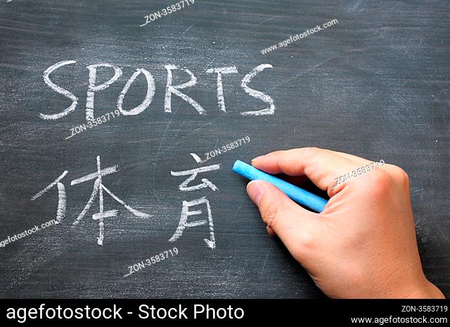 Sports - word written on a smudged blackboard with a Chinese translation, with a hand holding chalk writing