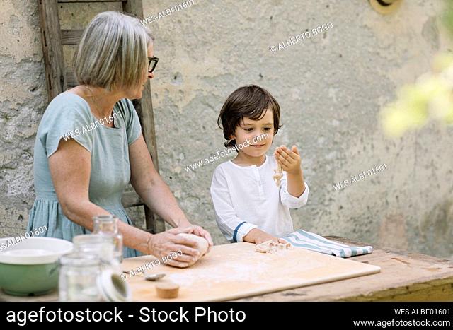Mature woman looking at grandson playing with dough in back yard