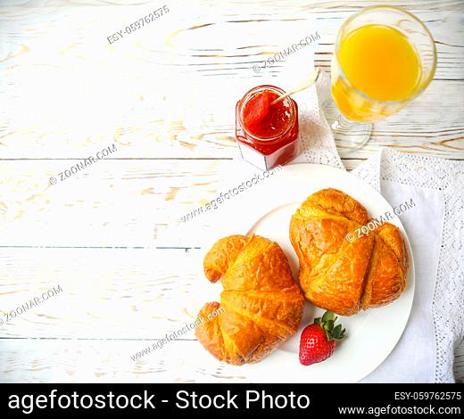 Two tasty croissants on the plate and strawberry jam on wooden background. Top view