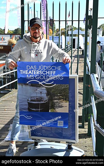 06 October 2022, Brandenburg, Potsdam: Boatman Artur Tuszynski attaches the advertising for the Jewish Culture and Theater Ship MS Goldberg in the marina