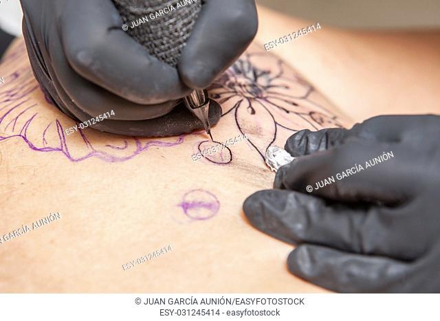 Tattoo artist applies tattoo to the shoulder blade of a woman. Closeup of pen ink machine injecting black ink