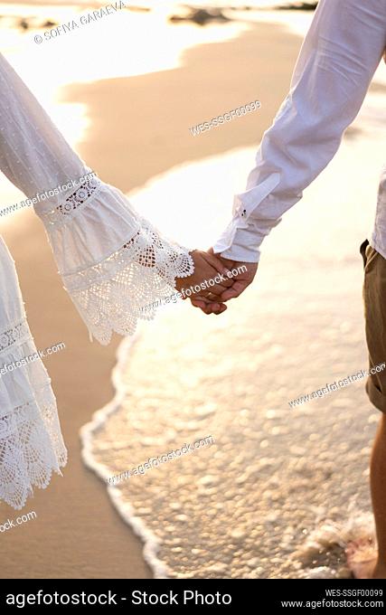 Young couple holding hands at beach on sunset