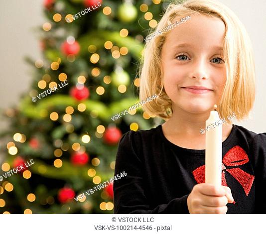 Girl (6-7) holding candlestick in front of Christmas tree