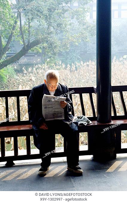 Elderly Chinese man reading newspaper in temple courtyard garden of the Wu Hou Shrine in city of Chengdu, Sichuan Province China
