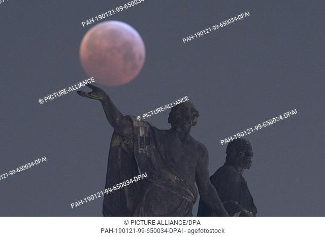 21 January 2019, Saxony, Dresden: As a red, so-called ""blood moon"" the full moon presents itself behind a Mattielli statue on the Catholic Court Church