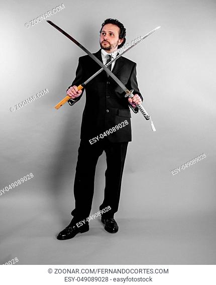 Businessman in black suit and armed japanese sword on gray background