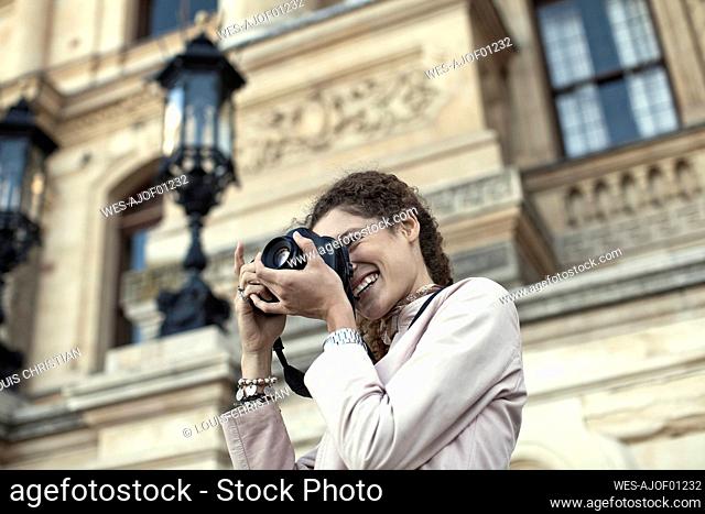 Young woman photographing through digital camera against building