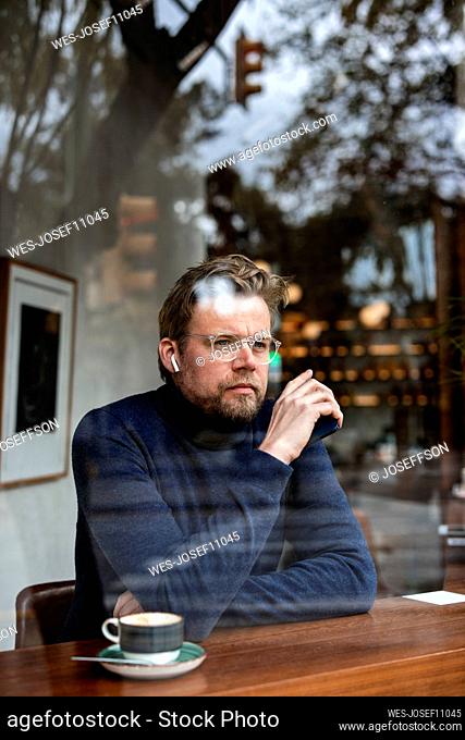 Thoughtful mature businessman in cafe seen through glass window