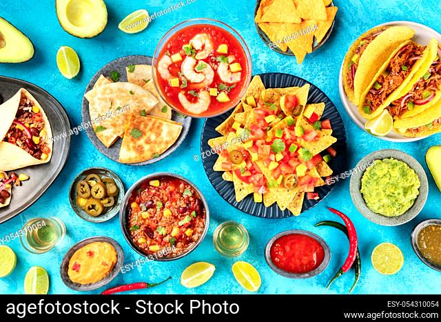 Mexican food, many dishes of the cuisine of Mexico, flat lay overhead shot from on a vibrant blue background. Nachos, tequila, guacamole, chili con carne