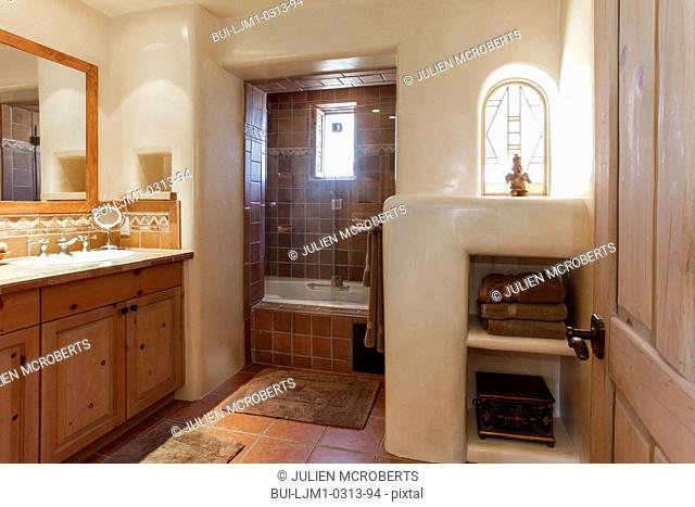 Brown cabinets and mirror with tiled bath in the background at bathroom; Santa Fe; New Mexico; USA