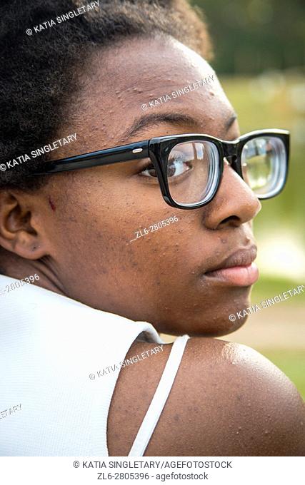 An African American teenager with black glasses is looking over her shoulders . Her white bra strap is showing. She looks thoughtful and sad