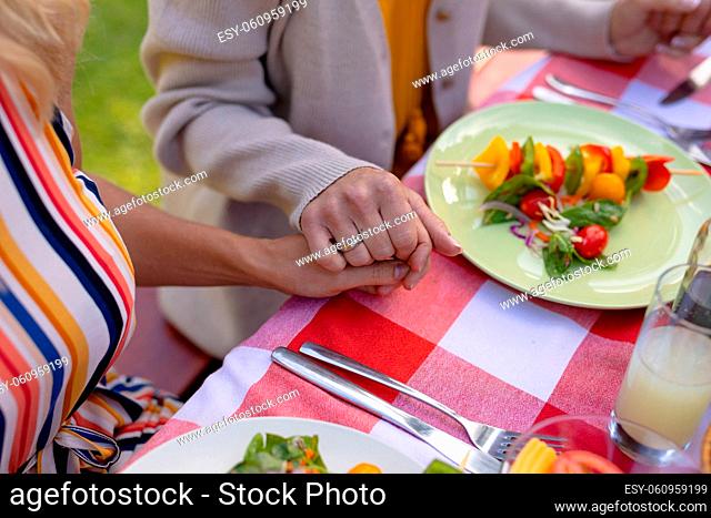 Midsection of caucasian mother and daughter holding hands praying at dining table