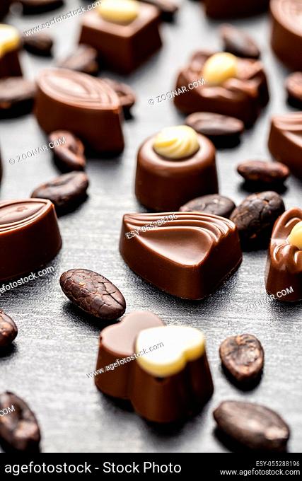 Various chocolate pralines and cocoa beans on black table