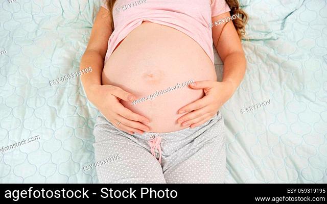 Top view of pregnant woman lying on hospital bed touching and stroking her big belly. Concept of pregnancy, preparing and expecting child