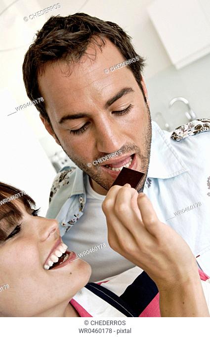 Close-up of a young woman feeding chocolate to a young man