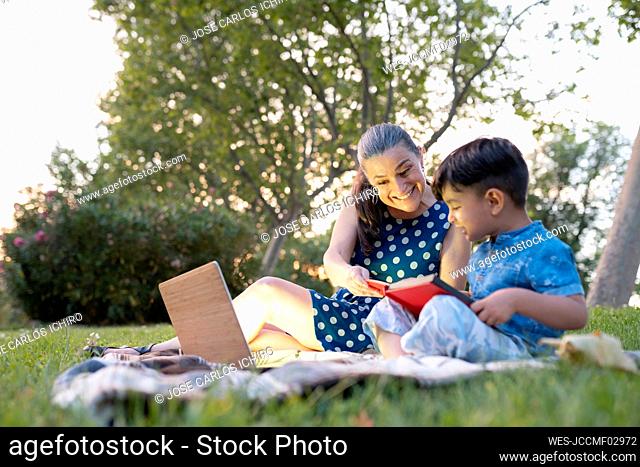 Smiling woman assisting grandson reading story book in public park
