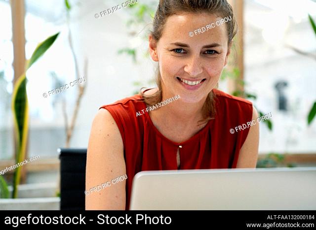 Businesswoman looking at the camera while using laptop at office