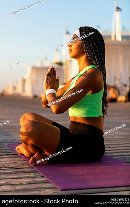 Young sportswoman with hands clasped practicing yoga on boardwalk