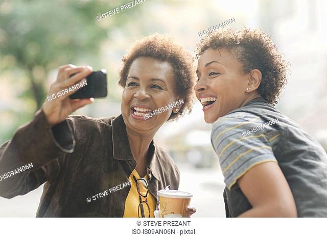 Two mature female friends taking smartphone selfie on street