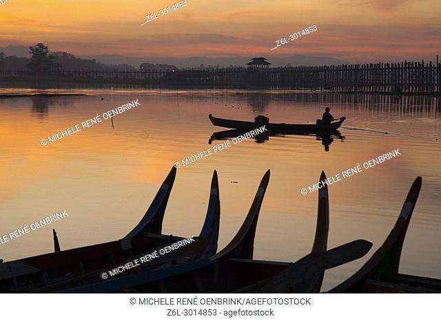sunrise over the lake with fishermen on boats fishing in the lake near wooden foot bridge U Bein Bridge crossing the Taungthaman Lake near Amarapura in Mandalay