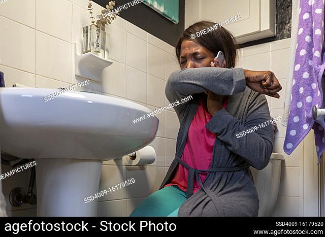 Young coughing woman in the bathroom feeling ill using Tele-medicine to communicate with a doctor