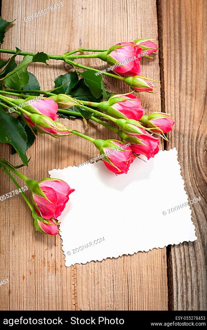 White card and pink roses on a wooden background