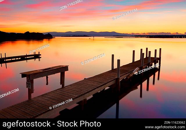 Rustic old timber jetty with old basin on calm waters at sunrise