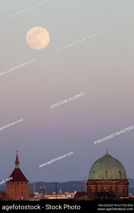 07 April 2020, Bavaria, Nuremberg: The moon rises as a so-called supermoon, in the foreground the White Tower (l) and the dome of the church St