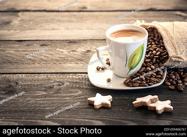 Coffee beans coming out from a small burlap sack and cup of hot coffee on a rustic black wooden table