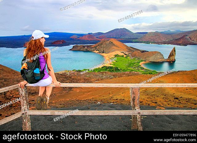 Young woman enjoying the view of Pinnacle Rock on Bartolome island, Galapagos National Park, Ecuador. This island offers some of the most beautiful landscapes...