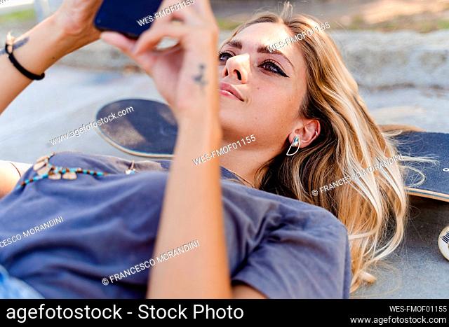 Beautiful woman using smart phone while lying on skateboard over road