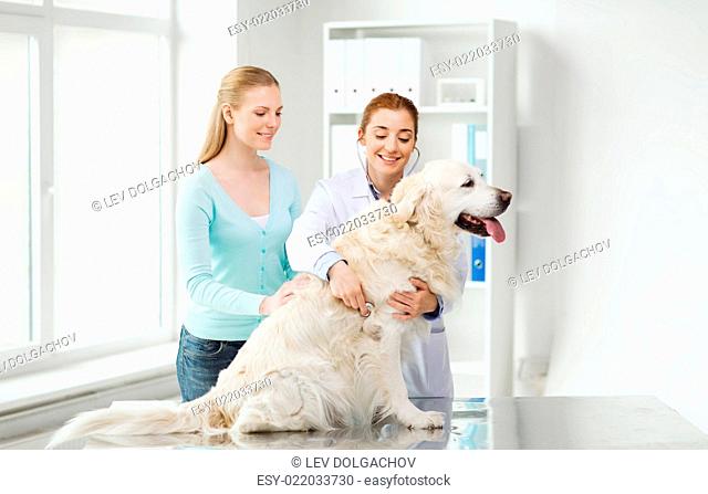 medicine, pet, animals, health care and people concept - happy woman and veterinarian doctor with stethoscope checking up golden retriever dog at vet clinic