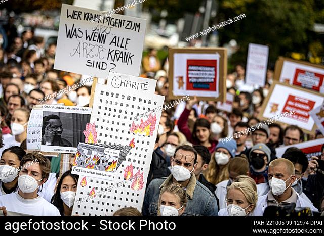 05 October 2022, Berlin: Doctors stand with a sign showing a burning Charite ward building during a one-day warning strike by the Marburger Bund at Charité