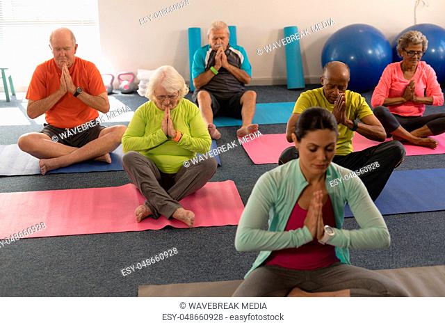 Senior people doing yoga with female trainer in fitness studio
