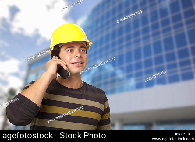 Handsome hispanic male contractor on cell phone in front of corporate building