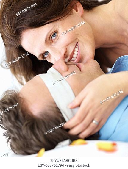 Closeup portrait of a smiling woman caressing her blindfolded husband on the bed